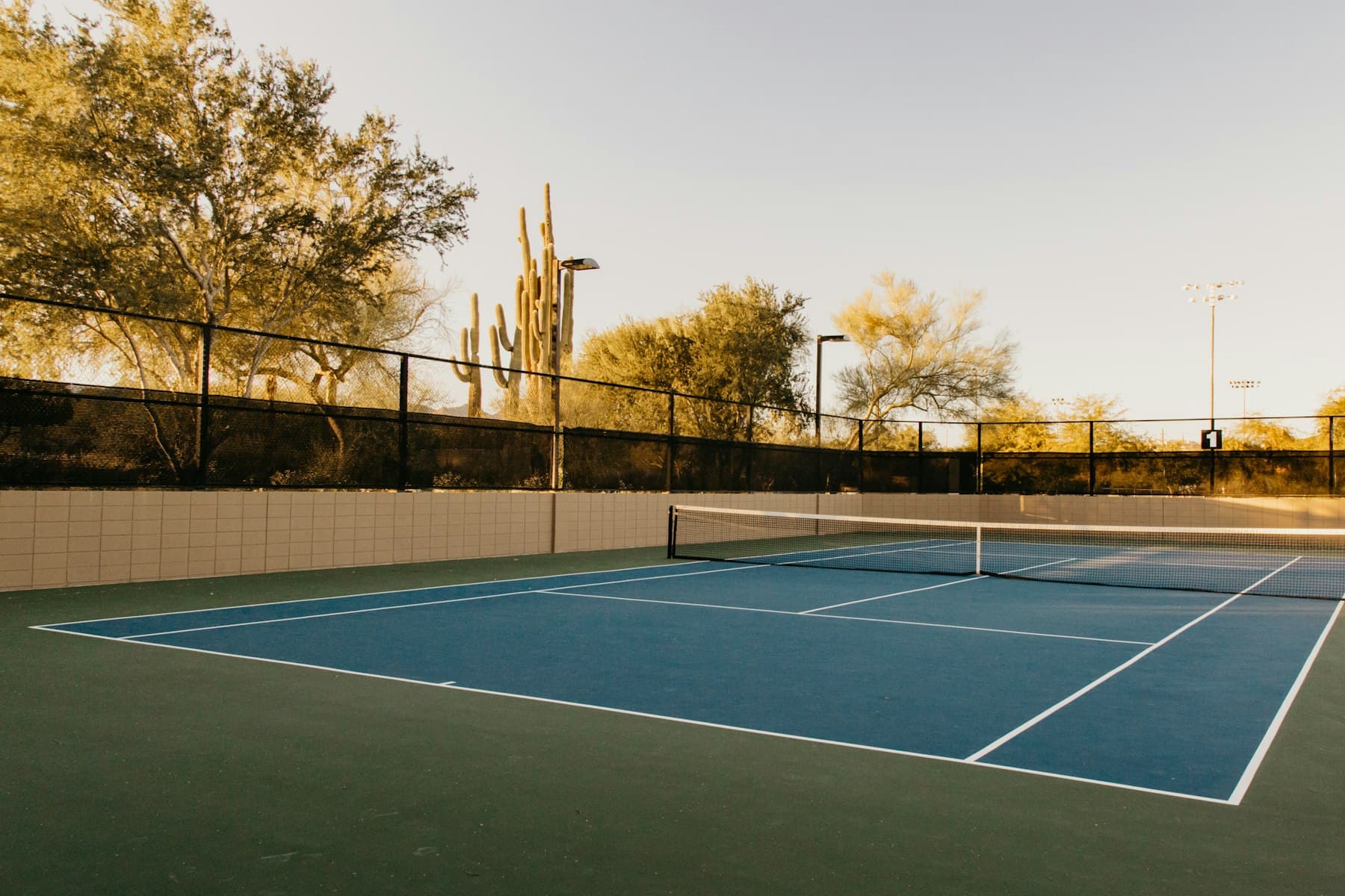 A blue hard tennis court at golden hour with warm Dubai light