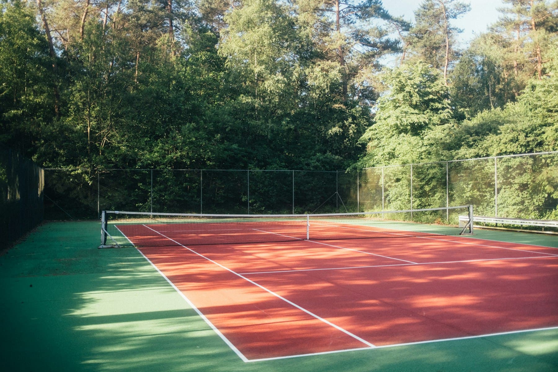 An outdoor resort tennis court framed by greenery in the afternoon sun