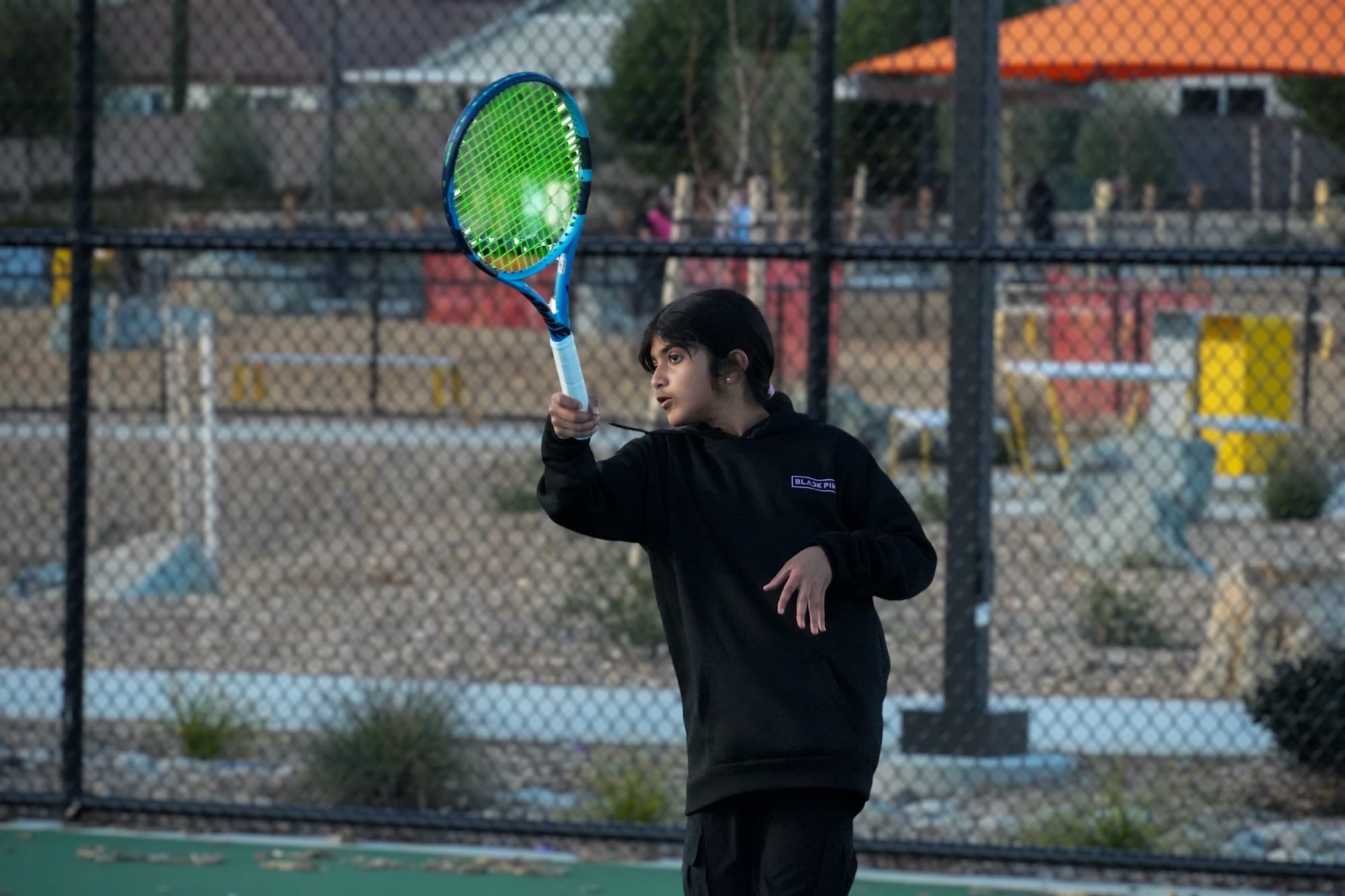 A young player focusing on her swing during an evening kids tennis class