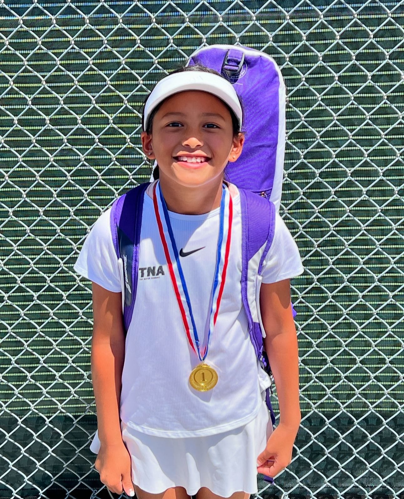A young TNA Pro Academy player in a TNA shirt smiling with her first-place medal