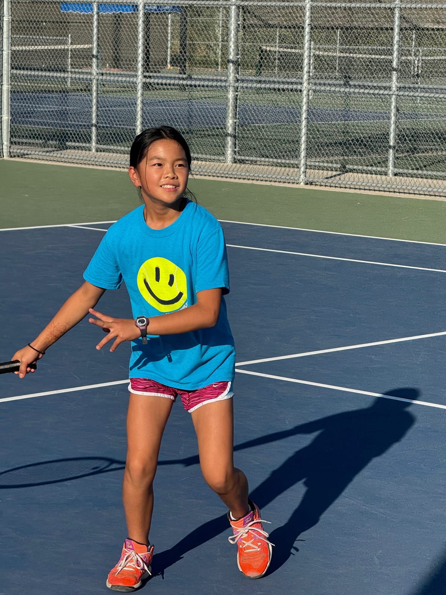 A junior player smiling as she prepares a forehand during a kids tennis session